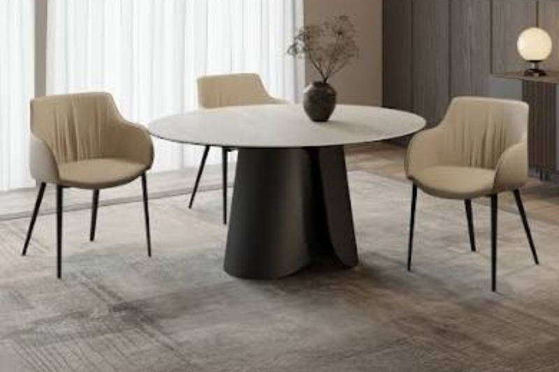 Tavolo rotondo di design con piano chiaro e base scultorea scura, circondato da poltroncine beige in un living luminoso