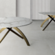 Tavolo rotondo allungabile con piano in marmo e base in metallo oro, con la versione ovale estesa sullo sfondo
